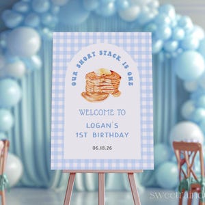 Puede incluir: Un cartel a cuadros azules y blancos con el texto "Our Short Stack Is One" y una ilustración de acuarela de una pila de panqueques. El cartel también dice "Welcome to Logan's 1st Birthday 06.18.26".