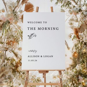 Może przedstawiać: Biały znak powitalny z czarnym tekstem, kt&oacute;ry brzmi "Witamy w The Morning After, świętując Allison & Logan 11.05.24". Znak stoi na drewnianym sztalugach przed kompozycją kwiatową.