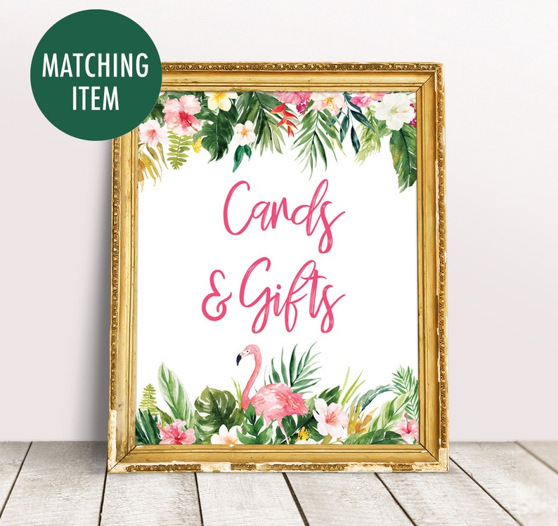 May include: A gold framed sign with a white background and pink text that says "Cards & Gifts". The sign is decorated with tropical leaves and flowers, including a pink flamingo.