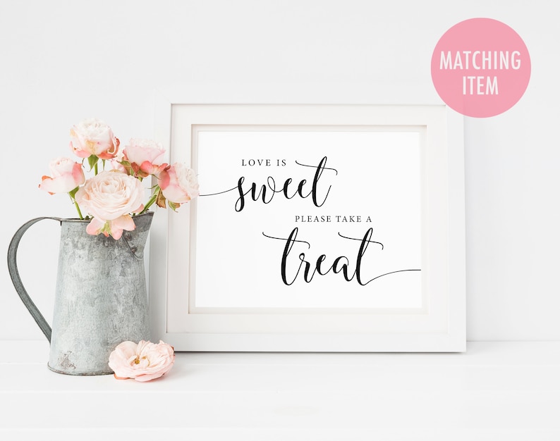 May include: White framed sign with black calligraphy that reads "Love is sweet, please take a treat". The sign is sitting on a white surface with a pitcher of pink flowers.