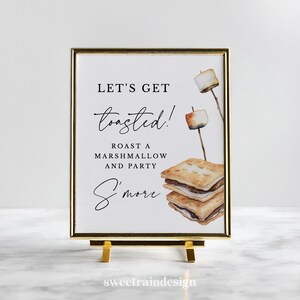 May include: A framed sign with gold trim and a gold easel. The sign reads "Let's Get Toasted! Roast a Marshmallow and Party S'more." Watercolor illustrations of toasted marshmallows on sticks and s'mores are featured on the sign.