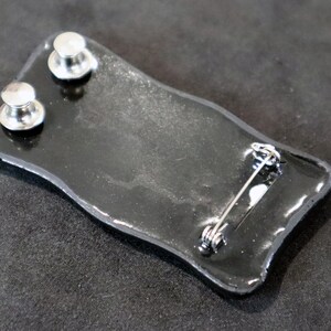 May include: Black enamel pin with a silver pin back and two silver posts on the back.
