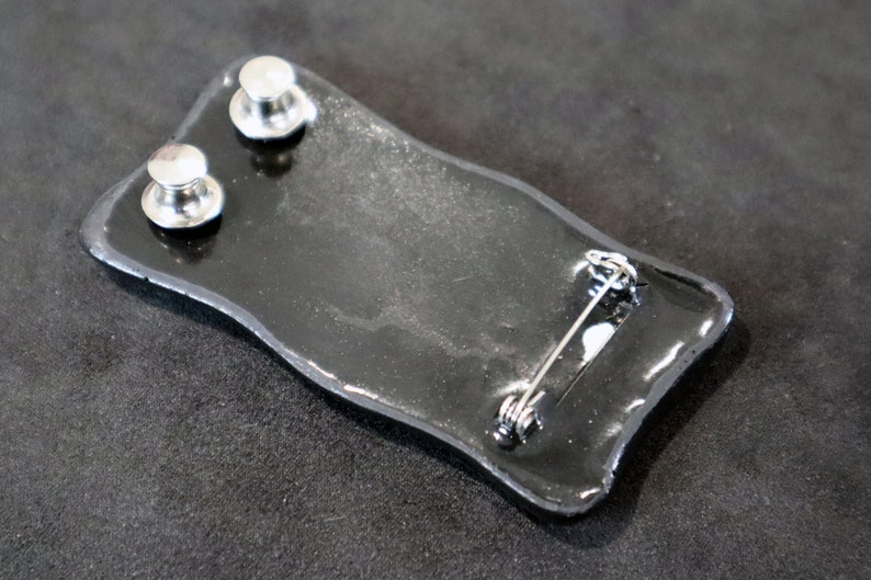 May include: Black enamel pin with a silver pin back and two silver posts on the back.