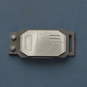 May include: A rectangular, metallic-looking device with a gray border. The center section is silver with geometric designs, including a rectangle and two parallel lines. Two circular rivets are on the left side, and a rectangular loop is on the right.