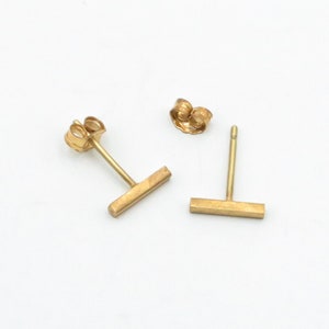 May include: A pair of gold bar stud earrings. The earrings are simple and minimalist, with a straight bar design.
