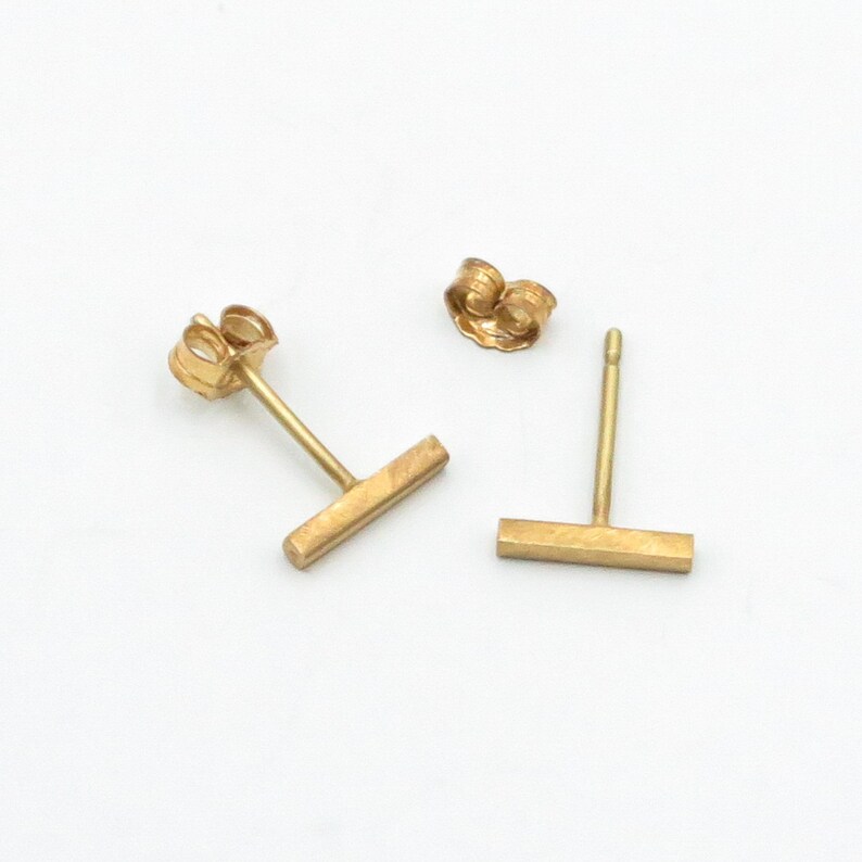May include: A pair of gold bar stud earrings. The earrings are simple and minimalist, with a straight bar design.