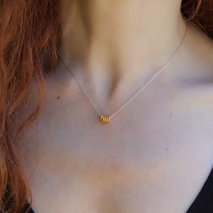 Peut inclure: Un collier en chaîne argent avec un groupe de cinq anneaux dorés qui pendent.