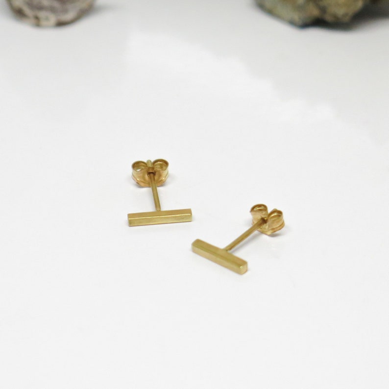 May include: A pair of gold bar stud earrings. The earrings are simple and minimalist, with a straight bar design.