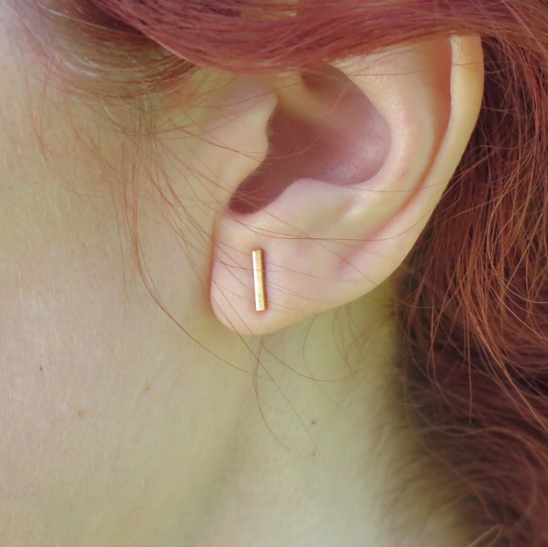 May include: A pair of gold bar stud earrings. The earrings are simple and minimalist, and they are perfect for everyday wear.