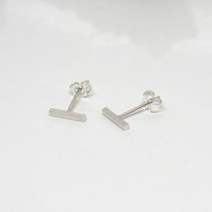 May include: A pair of silver bar stud earrings. The earrings are simple and minimalist, with a straight bar design.