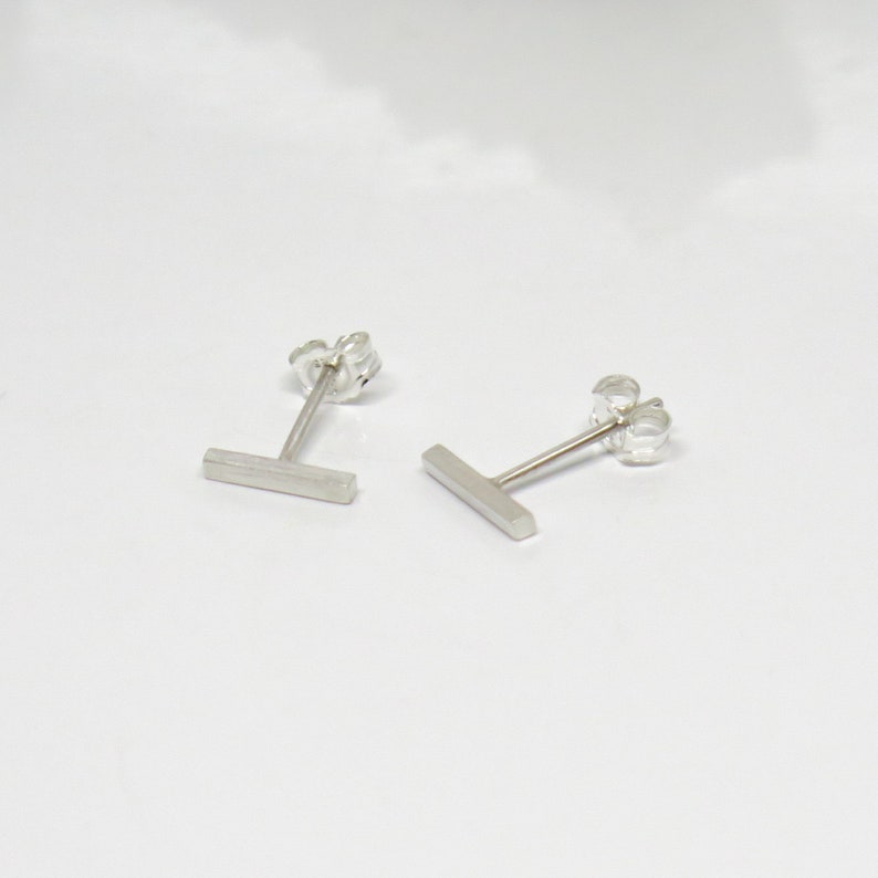 May include: A pair of silver bar stud earrings. The earrings are simple and minimalist, with a straight bar design.