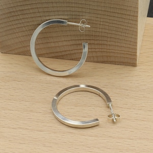 May include: A pair of silver hoop earrings with a brushed finish. The earrings are simple and elegant, and they would make a great gift for any occasion.