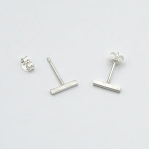 May include: A pair of silver bar stud earrings. The earrings are simple and minimalist, with a brushed finish.