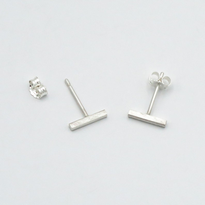 May include: A pair of silver bar stud earrings. The earrings are simple and minimalist, with a brushed finish.