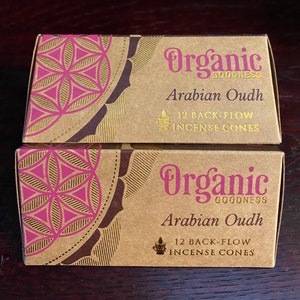 May include: Two boxes of Organic Goodness Arabian Oudh backflow incense cones. The boxes are brown with a pink and gold geometric design. Each box contains 12 cones.