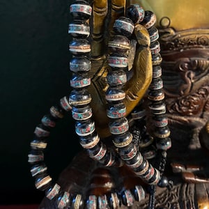 May include: Two black and white prayer beads with turquoise and gold accents. The beads are strung on a black cord with a black tassel.