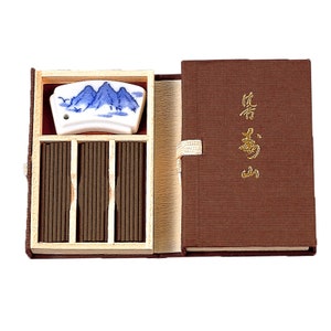 May include: A wooden box containing incense sticks and a ceramic incense holder with a blue and white mountain design. The box is closed and has a brown cover with gold lettering that reads "香道".