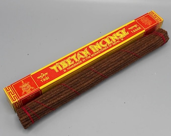 Può includere: Una scatola rettangolare di incenso tibetano con un design giallo e rosso e un fascio di bastoncini di incenso marroni legati con uno spago rosso. La scatola recita "Tibetan Incense" in lettere gialle.