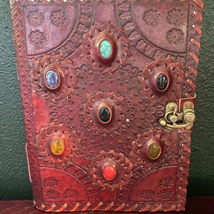 May include: A brown leather journal with a decorative design and colorful gemstones. The journal has a clasp closure and is perfect for writing or journaling.