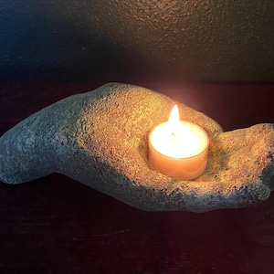 May include: A teal green hand-shaped candle holder with a lit tea light candle inside.