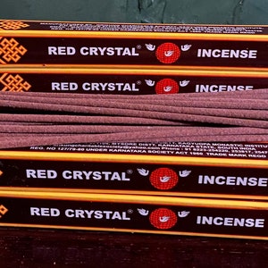 May include: A stack of four boxes of "Red Crystal" incense, with a bundle of incense sticks on top. The boxes are yellow with red and gold accents, and the text "INCENSE" is visible. The incense sticks are a reddish-brown color.