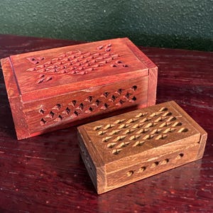 May include: Two wooden boxes with intricate carved designs. The larger box is red and the smaller box is brown.
