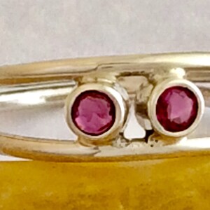 May include: A silver ring with two pink gemstones set in the band. The ring is double-banded and the gemstones are set in a simple, modern style.