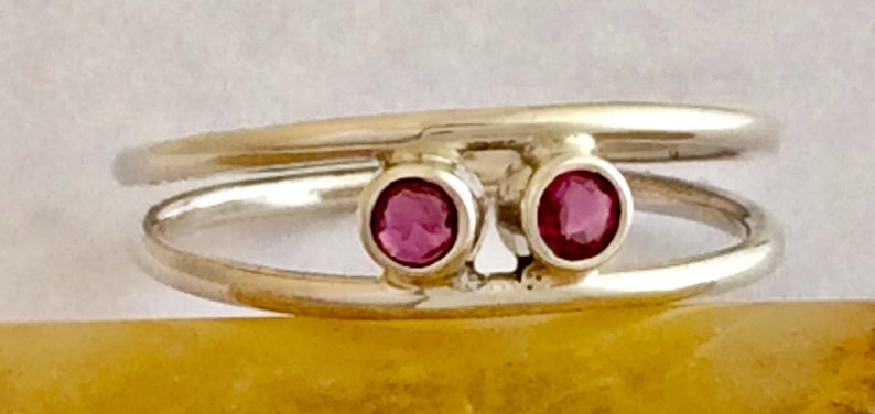May include: A silver ring with two pink gemstones set in the band. The ring is double-banded and the gemstones are set in a simple, modern style.