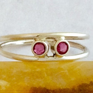 May include: A silver ring with two pink gemstones set in the band. The ring is designed with two bands that are intertwined.