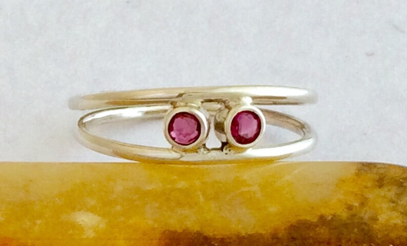 May include: A silver ring with two pink gemstones set in the band. The ring is designed with two bands that are intertwined.