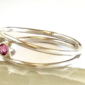 May include: A silver ring with a delicate, twisted band and three pink gemstones.