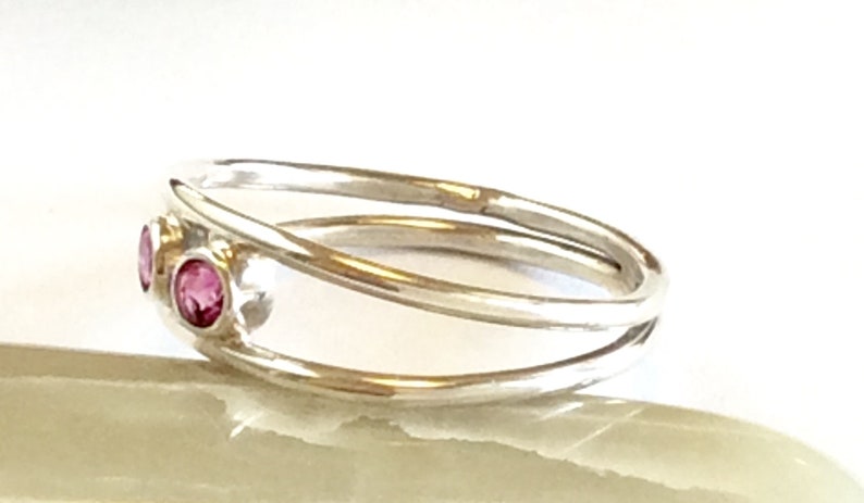 May include: A silver ring with a delicate, twisted band and three pink gemstones.