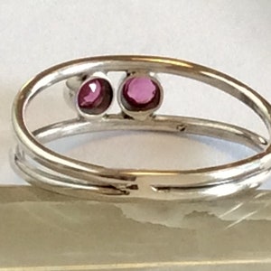 May include: A silver ring with two small, round, pink gemstones set in the band.