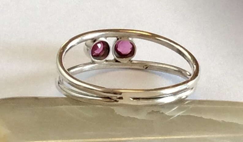 May include: A silver ring with two small, round, pink gemstones set in the band.
