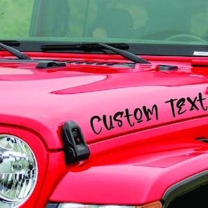 May include: A red Jeep Wrangler with a black custom text decal on the hood that says "CUSTOM TEXT".