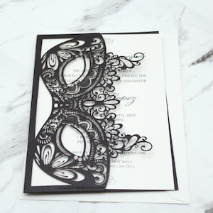May include: Black laser cut invitation with a delicate, intricate mask design. The invitation text reads "Celebrate the daughter Lopez 6th, 2019" and includes a phone number and website address.