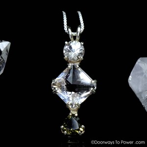 May include: A silver pendant necklace with three clear, faceted gemstones. The top stone is round, the middle is a diamond shape, and the bottom is a teardrop shape. The pendant hangs from a delicate silver chain against a black background.