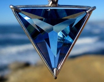 May include: A silver pendant with a blue crystal in the shape of a triangle. The pendant is hanging from a silver chain.