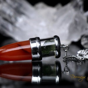 May include: A silver and red carnelian crystal pendulum with a green crystal inside a glass vial. The pendulum is attached to a silver chain. The text "Doorways to Power THE KEYS WITHIN" is visible in the image.
