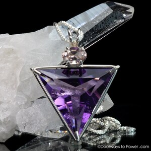May include: A silver pendant featuring a triangular amethyst gemstone with a smaller pink gemstone at the top. The pendant is on a silver chain.