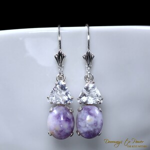 May include: A pair of silver dangle earrings with a purple and white gemstone and a clear triangular crystal. The earrings have a delicate design and are perfect for adding a touch of elegance to any outfit.