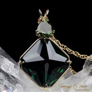 Puede incluir: Un collar con un colgante de oro con una gran piedra preciosa verde oscura facetada en un engaste cuadrado. Una piedra preciosa verde triangular m&aacute;s peque&ntilde;a se encuentra encima de la m&aacute;s grande.
