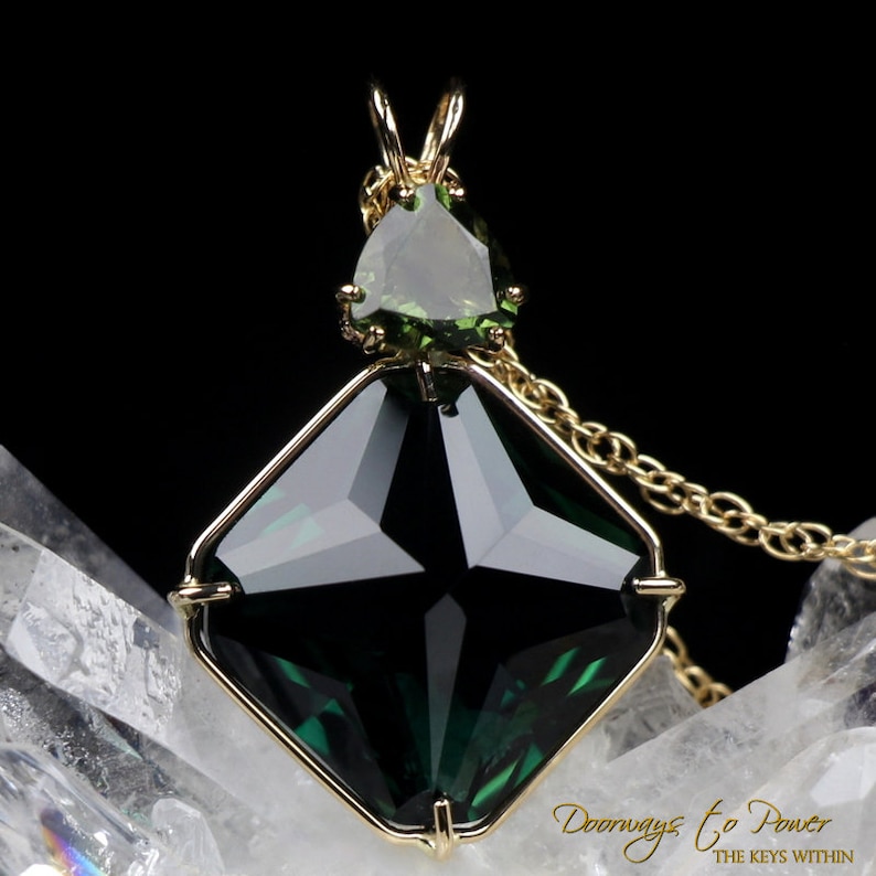 Puede incluir: Un collar con un colgante de oro con una gran piedra preciosa verde oscura facetada en un engaste cuadrado. Una piedra preciosa verde triangular m&aacute;s peque&ntilde;a se encuentra encima de la m&aacute;s grande.