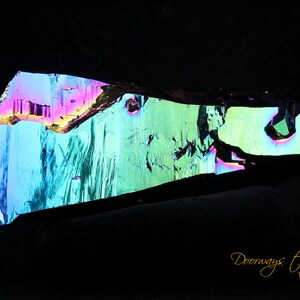 May include: A large, iridescent crystal with a green, blue, and purple color scheme. The crystal is shaped like a long, thin blade and has a rough, textured surface.