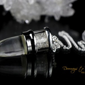 May include: A clear crystal pendulum with a silver-colored metal cap and chain. The pendulum has a bullet-like shape and is suspended on a silver chain with a small crystal ball at the end. The background is black with the text "Doorways to Power THE KEYS WITHIN".