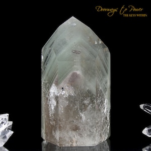 Puede incluir: Un cristal verde claro con una punta puntiaguda y una base plana. El cristal tiene un aspecto nublado y está rodeado de un fondo negro.