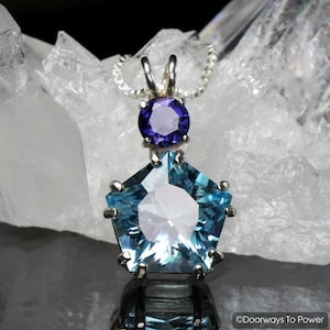 Puede incluir: Un colgante de plata con una piedra preciosa azul y transparente en forma de estrella y una piedra preciosa púrpura más pequeña encima.