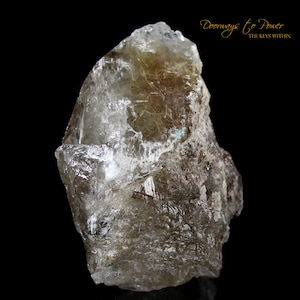 Puede incluir: Un gran cristal de cuarzo transparente con inclusiones marrones. El cristal tiene una superficie rugosa y natural y es translúcido. El cristal es una muestra natural y no está pulido.