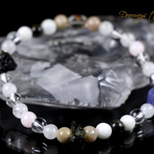 May include: A bracelet made of various stones, including clear quartz, white moonstone, pink rose quartz, brown tiger's eye, black obsidian, and blue sodalite. The bracelet is on a white crystal surface. The text "Doorways to Power" is visible in the upper right corner of the image.
