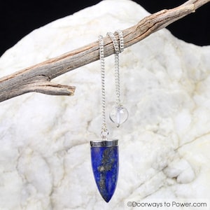 May include: A silver chain dangles from a branch, holding a clear quartz crystal ball and a blue lapis lazuli pendulum. The pendulum is pointed and has a silver top.